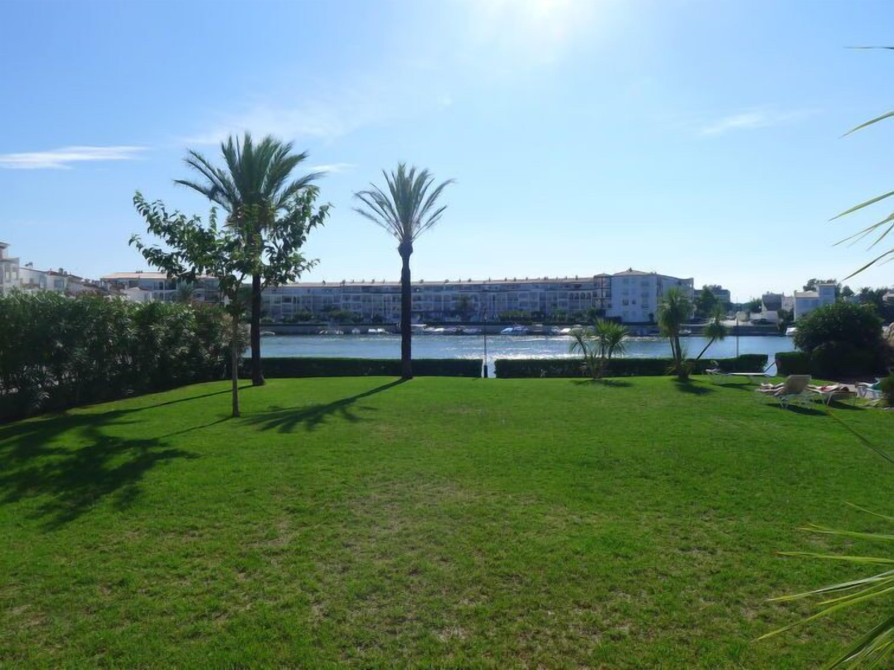 A grassy area with palm trees and a view of a large hotel building across a body of water.