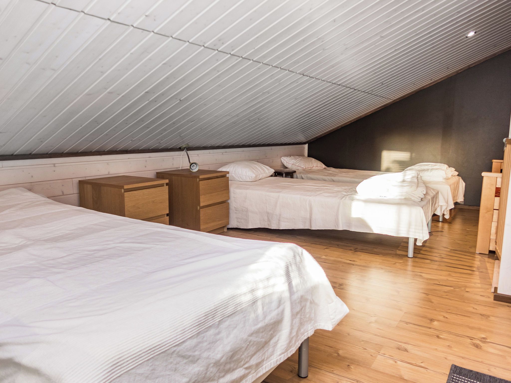 A dormitory-style room with two beds, wooden furniture, and a sloped ceiling.