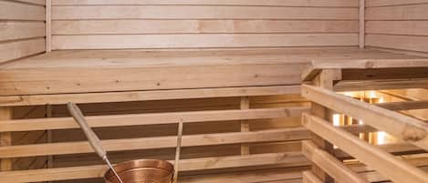 Een sauna met houten banken en een koperen emmer.