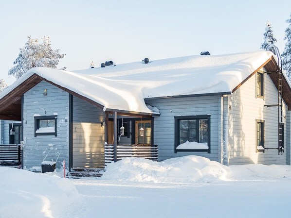 Een houten vakantiehuis met twee verdiepingen, een met sneeuw bedekte dak en een klein terras.