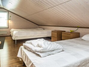 Een gezellige slaapkamer onder de dakpannen met twee bedden, houten hoofdeinden en een klein bureau met lamp.