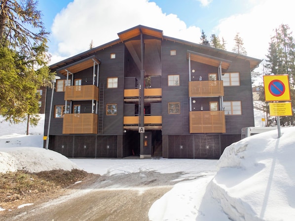 A multi-story building with balconies, a covered entrance, and a snow-covered ground.