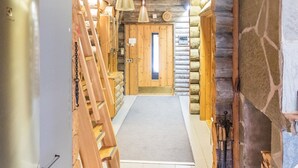 A log cabin interior with a wooden staircase, a central door, and hanging pendant lights.