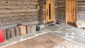 A log cabin with two wooden doors, a stone-paved entrance, and a red vehicle parked outside.