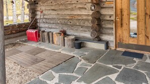 A log cabin with a stone-paved entrance, a wooden door, and a red suitcase on the left.