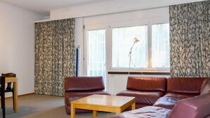 A living room with a brown leather sofa, a wooden coffee table, and a patterned curtain. - Allod Park Haus C E03 by Interhome (Davos)
