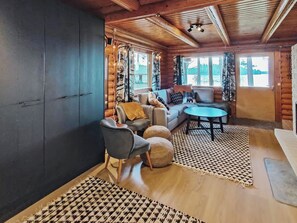 A log cabin interior with a sofa, chairs, a round table, and a large window with a view of trees and water. - Kuusela by Interhome (Soini)