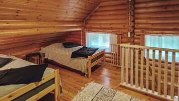 Una cabaña con dos camas de madera, un barandal blanco y una ventana con cortinas.