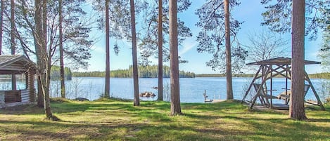 A lakeside cabin with a swing set and a dock extending into the water.