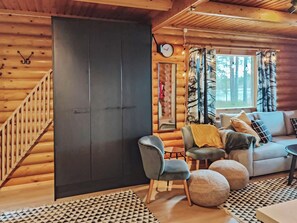 A log cabin interior with a staircase, a sofa, a chair, and a large window with curtains. - Kuusela by Interhome (Soini)