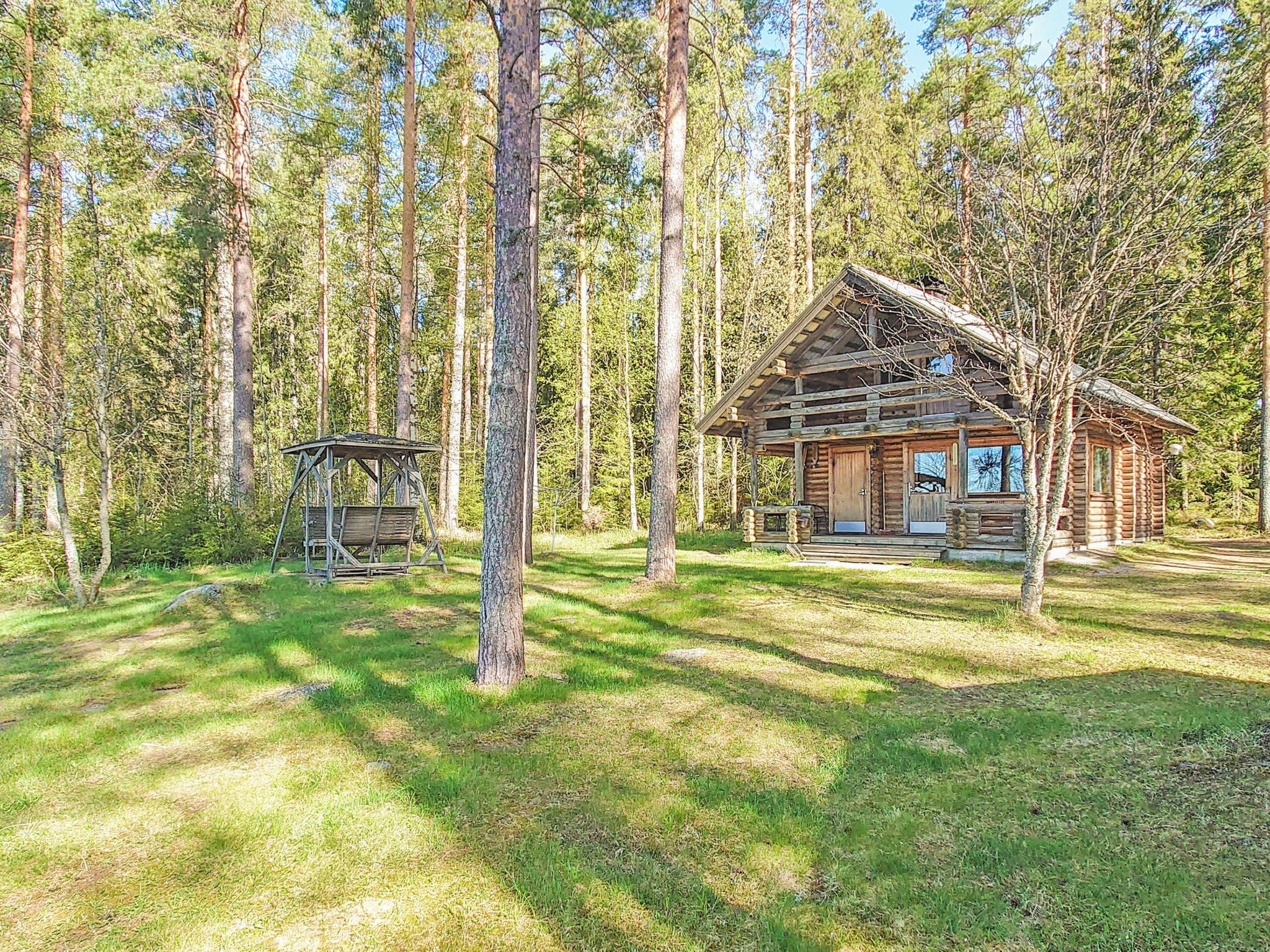 Mökki, jossa on kuisti ja pieni suoja, sijaitsee metsässä.