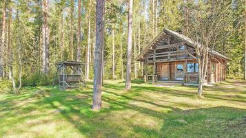 Mökki, jossa on kuisti ja pieni suoja, sijaitsee metsässä.