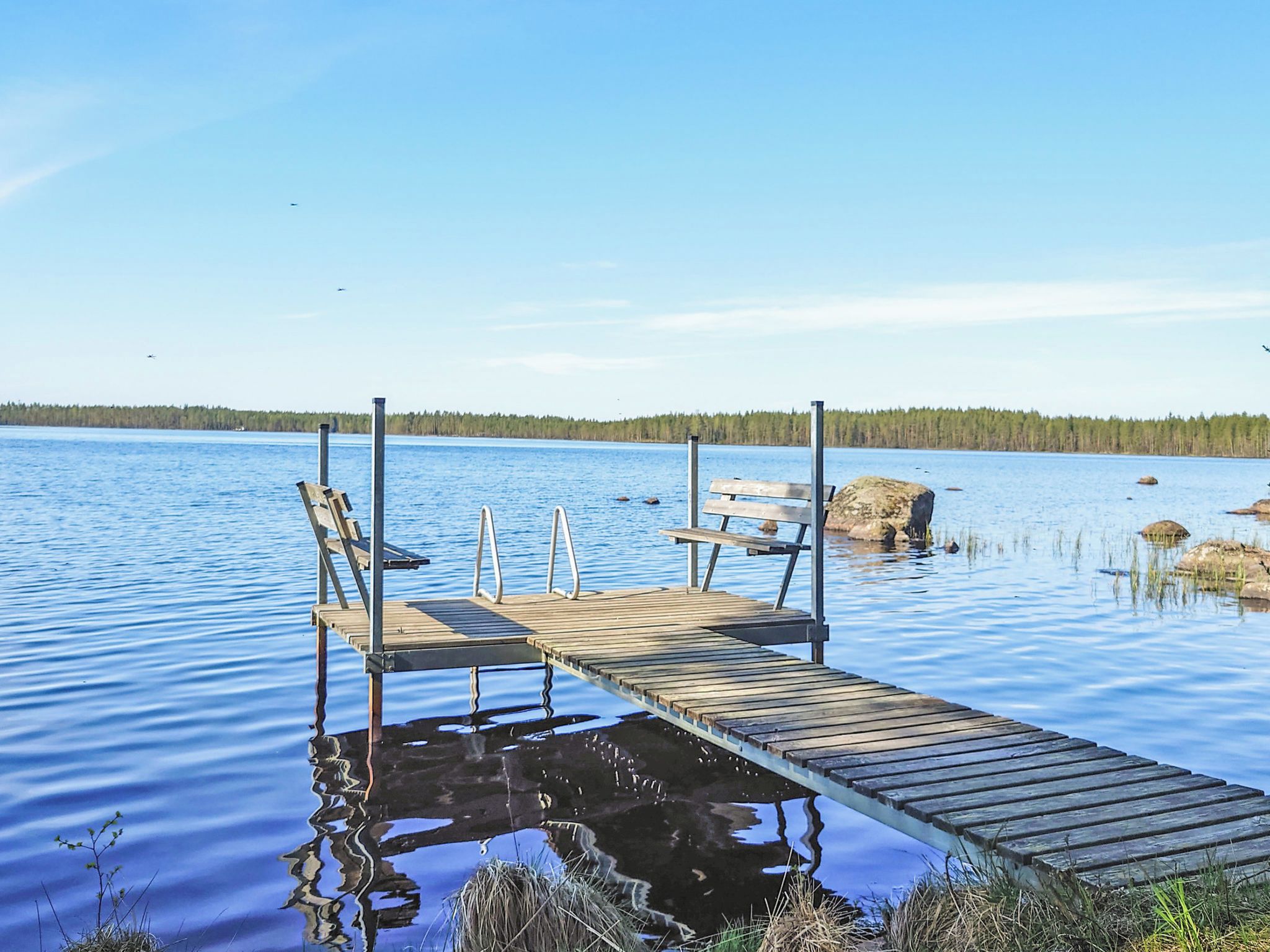 A wooden dock extending into calm water with a bench and a picnic table.