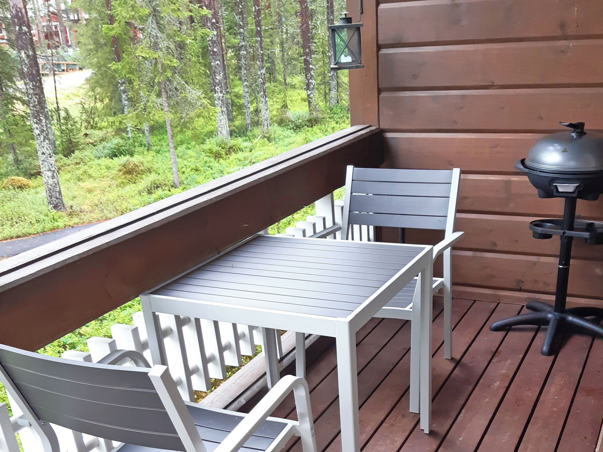 A wooden deck with a table and chairs, a grill, and a view of a forest.