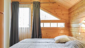 Une chambre confortable dans un chalet, avec un lit, deux fenêtres équipées de rideaux et un plafond en pente.