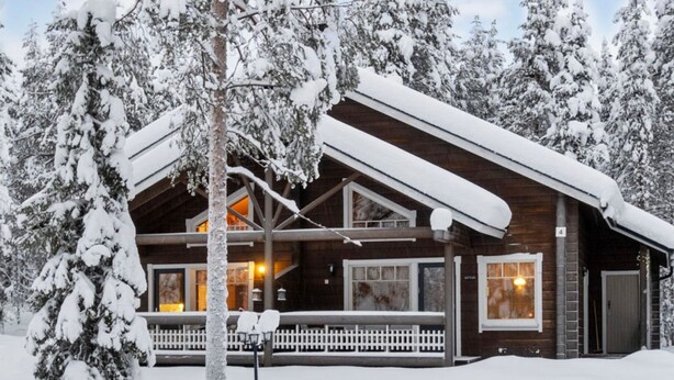 Une cabane en bois dotée d’un porche abrité, entourée d’arbres couverts de neige.