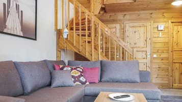 A modern living room with a grey sectional sofa, a wooden staircase, and a wooden ceiling.