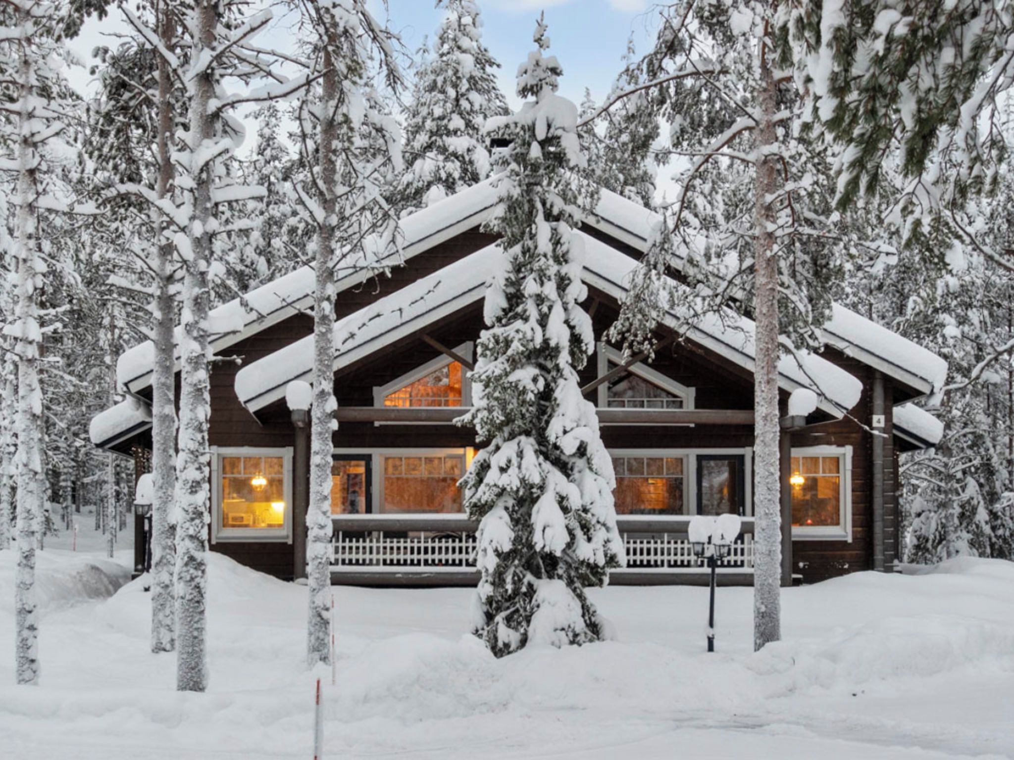 A log cabin with a porch, surrounded by snow-covered trees.