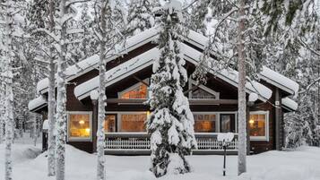 A log cabin with a porch, surrounded by snow-covered trees.
