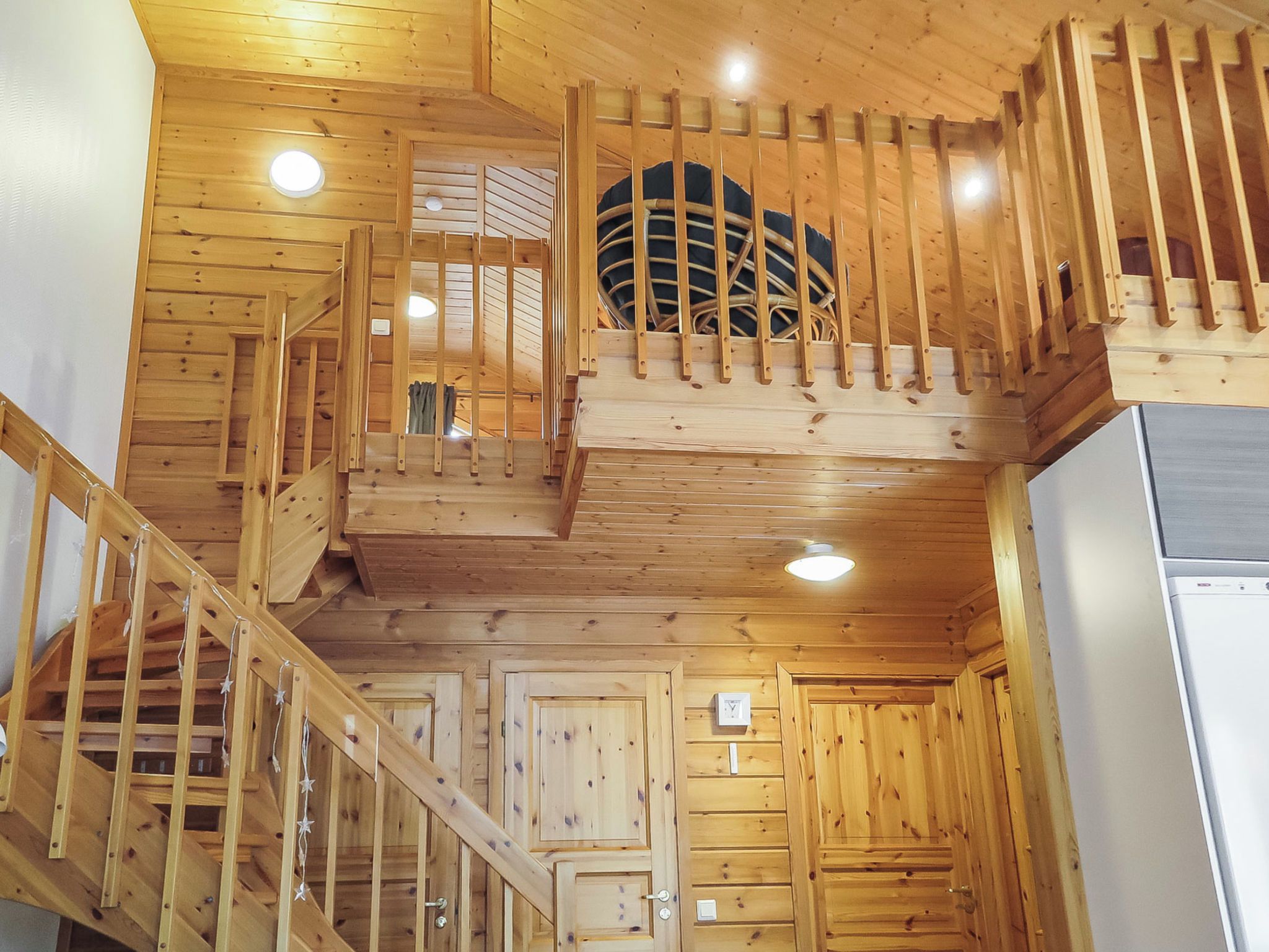 A wooden interior with a staircase, a kitchen area, and a window with blinds.