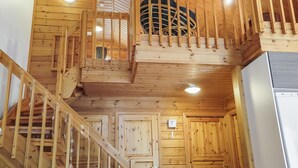Un intérieur en bois avec un escalier menant à un niveau supérieur, un coin cuisine et une horloge bien visible.