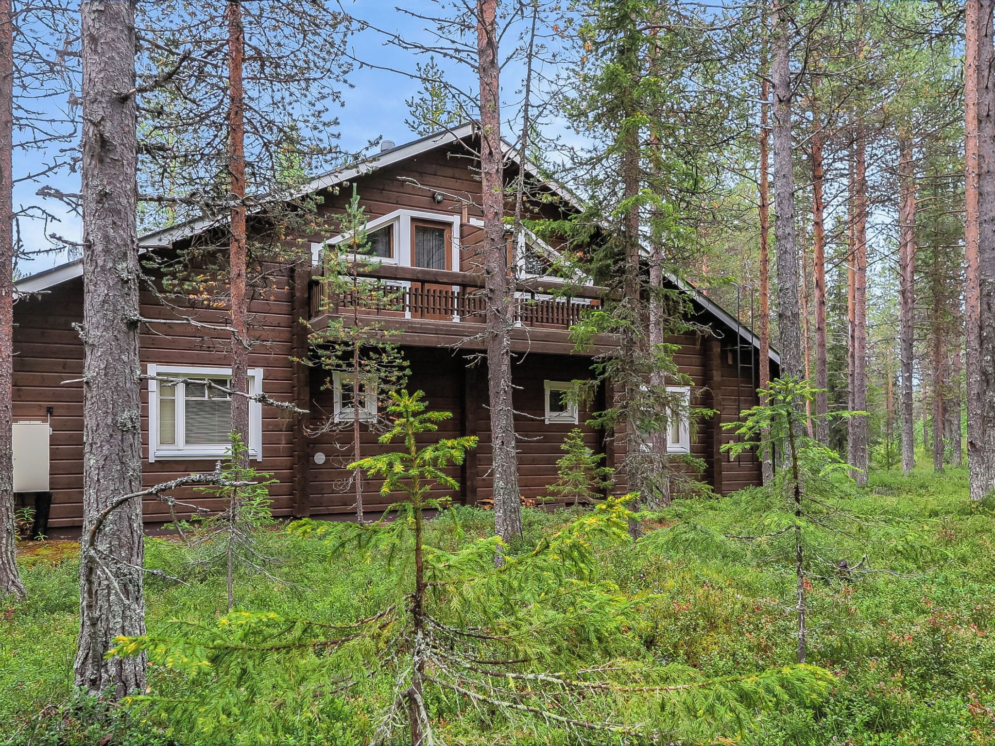 Eine zweistöckige Blockhütte mit Balkon, umgeben von dichtem Wald.