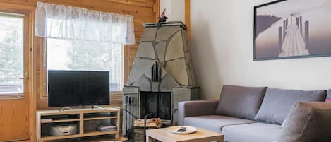 En hyggelig stue med en stenspejs, et fjernsyn, en sofa og et sofabord.