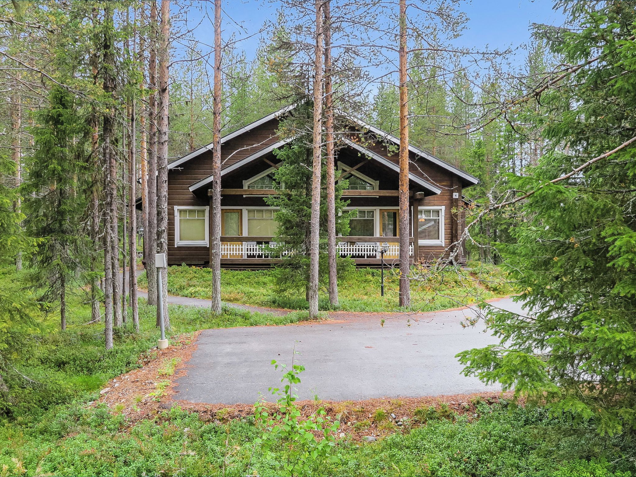A cabin with a porch, surrounded by tall trees and a clear sky.