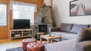 Un salon chaleureux avec une cheminée en pierre, un téléviseur, un canapé et deux poufs.