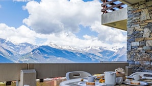 Un balcone con un tavolo apparecchiato per la colazione, con vista su un paesaggio montuoso.