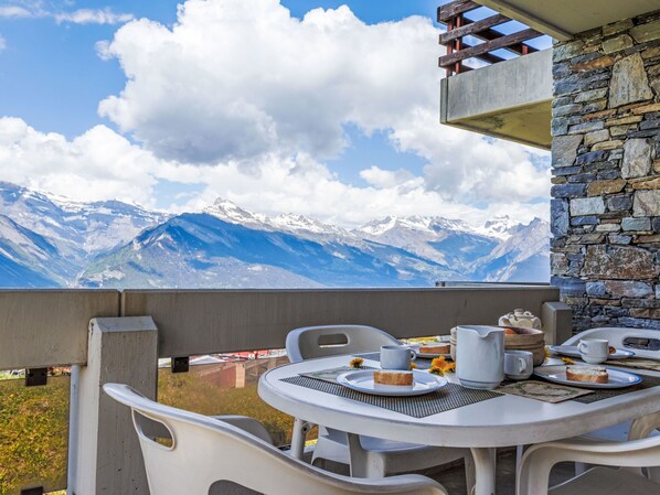 A balcony with a table set for breakfast, overlooking a mountainous landscape.
