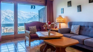 Un soggiorno accogliente con un divano, un tavolino in legno e vista sulle montagne innevate attraverso ampie finestre.
