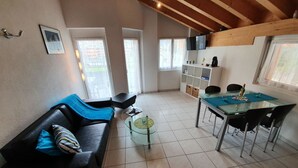 Een moderne woonkamer met een zwarte leren bank, een glazen salontafel, en een eethoek met een glazen tafel en stoelen.
