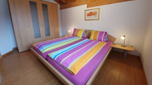 Een slaapkamer met een bed, een houten garderobe en een nachtkastje met een lamp.