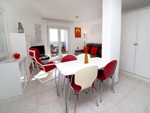 Un salon moderne avec une table à manger blanche, des chaises rouges, un canapé et un téléviseur.