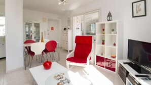 A modern living room with a red armchair, a white coffee table, and a TV stand with a flat-screen TV. - Playsol by Interhome (Calpe/Calp)