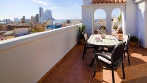 A rooftop terrace with a table and chairs, a view of the city and ocean, and a white building with arches. - Playsol by Interhome (Calpe/Calp)