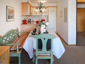 Un coin repas avec une table dressée pour deux personnes, un banc et une cuisine en arrière-plan.