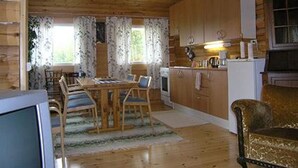 Interior de una cabaña de madera con comedor, cocina y un gran ventanal con cortinas.
