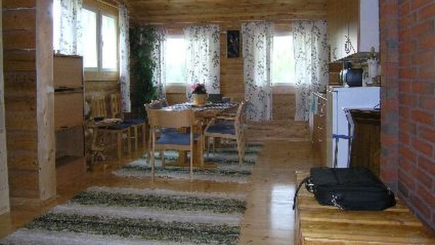 Un interior de madera con zona de comedor, cocina y escalera.