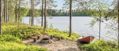 A lakeside campsite with a fire pit, a boat, and surrounding greenery.