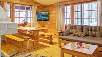 A cozy cabin interior with wooden walls, a television, a sofa, and a dining table.