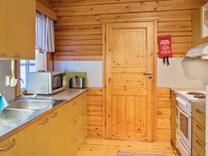 A compact kitchen with wooden cabinets, a microwave, a kettle, and a stove.