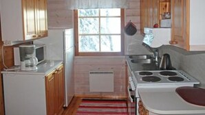 A compact kitchen with wooden cabinets, a refrigerator, a stove, and a window with a view of trees. - Karpalo by Interhome (Kittilä)