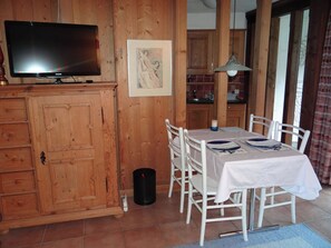 Un coin repas avec une table dressée pour quatre personnes, des meubles en bois, un téléviseur et un tableau encadré au mur.