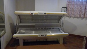 Un lettino abbronzante in una stanza con pavimento piastrellato e una finestra con tenda floreale.