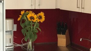 A kitchen with white cabinets, a red backsplash, a sink, and a vase with sunflowers on the counter. - Apartment Channa by Interhome (Saas-Almagell)