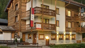 A multi-story wooden building with balconies, a restaurant sign, and a sign indicating a ski lift service. - Apartment Channa by Interhome (Saas-Almagell)