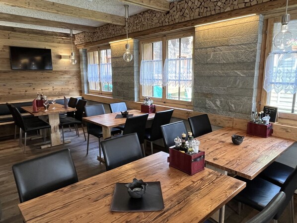 A restaurant with wooden tables and chairs, stone walls, and large windows.