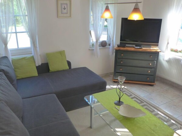Una sala de estar moderna con un sofá gris, una mesa de centro de vidrio y un televisor sobre un mueble de madera.